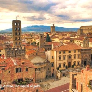 K&ouml;nnte beinhalten: Panoramablick auf Arezzo, Italien, eine historische Stadt mit Terrakotta-D&auml;chern, hohen T&uuml;rmen und einem gro&szlig;en, offenen Platz. Die Stadt ist von sanften H&uuml;geln und einem bew&ouml;lkten Himmel umgeben.