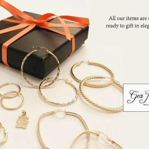 May include: A set of gold hoop earrings in various sizes and styles, including a pair of square earrings. The earrings are displayed on a black gift box with a red ribbon. The text "Gea Jewelry" is visible in the image.