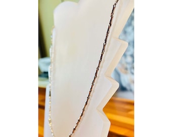 Op de afbeelding: Een zilveren ketting met een delicaat, gekoppeld ontwerp. De ketting is gemaakt van kleine, ronde schakels die met elkaar verbonden zijn om een ​​continue lus te vormen.