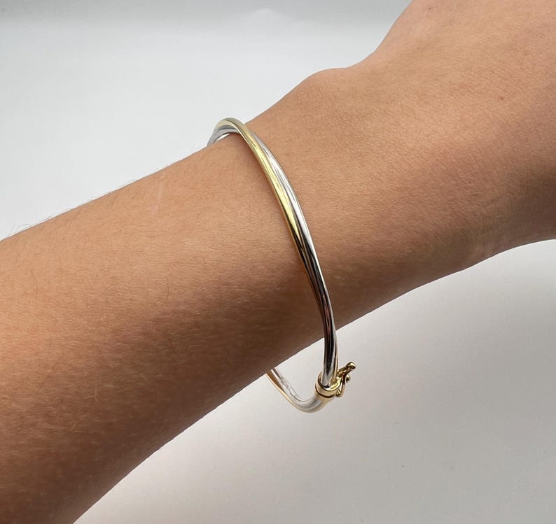 May include: A silver and gold bangle bracelet with a hinged clasp.