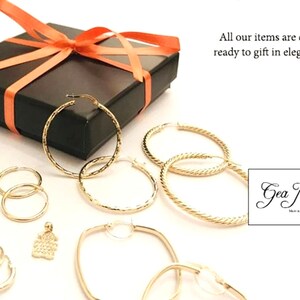 K&ouml;nnte beinhalten: Ein Set goldener Creolen in verschiedenen Gr&ouml;&szlig;en und Stilen, verpackt in einer schwarzen Geschenkbox mit einem korallenfarbenen Band. Die Ohrringe sind bereit zum Verschenken. Die Box enth&auml;lt auch einen kleinen goldenen Anh&auml;nger mit einem strukturierten Design. Das Bild enth&auml;lt den Text "Gea Jewelry".