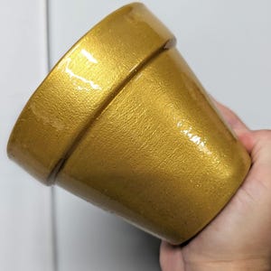 May include: A gold-colored ceramic flower pot with a shiny, metallic finish.