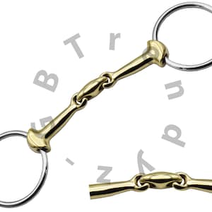 Pode incluir: Um freio de cavalo dourado com dois anéis soltos. O freio tem uma embocadura de dupla articulação.