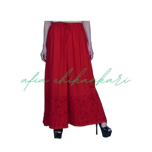May include: A red long skirt with a drawstring waist and floral embroidery. The skirt is made of a soft, flowing fabric.
