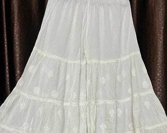 May include: White cotton palazzo pants with embroidered floral details. The pants have a tiered design with multiple layers.