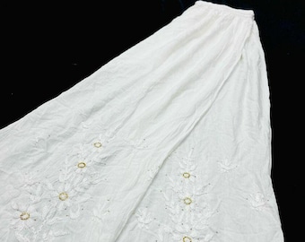 May include: White cotton skirt with delicate floral embroidery and gold accents. The skirt has a flowing silhouette and a lace trim.