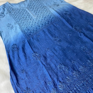May include: A blue ombre dress with intricate floral embroidery. The dress transitions from a light blue at the top to a deep blue at the bottom. The embroidery is concentrated around the neckline, sleeves, and hem, creating a detailed and elegant look.