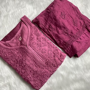 May include: A two-piece pink embroidered outfit with a long-sleeved top and matching trousers. The top has a V-neck and a small tag with the number "42" on it.