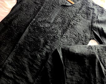 May include: A black long-sleeved tunic and matching trousers set featuring a crinkled fabric texture. The tunic has a round neckline and intricate tonal black floral embroidery across the chest and sleeves, with similar embroidery on the trousers.