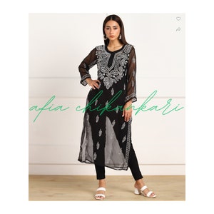 May include: A black sheer tunic with silver embroidery featuring a paisley design. The tunic has a V-neckline and long sleeves. The model is wearing black trousers and white sandals.