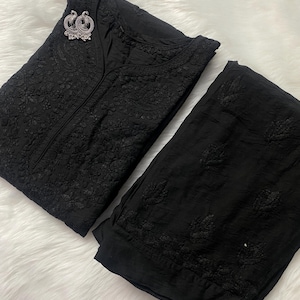 May include: Black embroidered kurta and matching pants set. The kurta features intricate floral patterns and a V-neckline. A silver-toned peacock brooch adorns the kurta. The set is made of a soft, flowing fabric, perfect for a comfortable and stylish look.