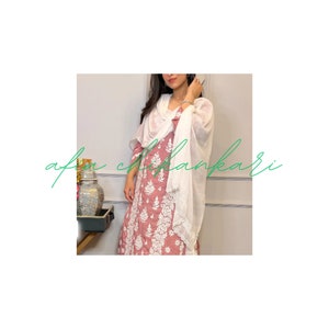 May include: A woman wearing a pink and white embroidered dress with a white scarf. The dress has a floral pattern and the scarf is draped around her neck.