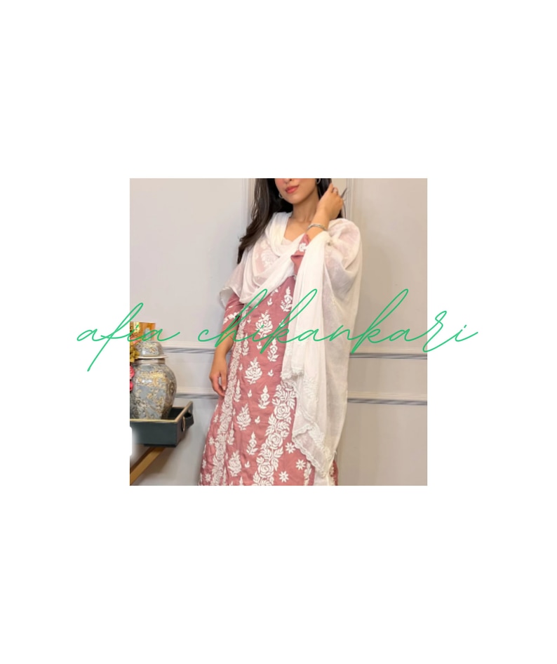May include: A woman wearing a pink and white embroidered dress with a white scarf. The dress has a floral pattern and the scarf is draped around her neck.