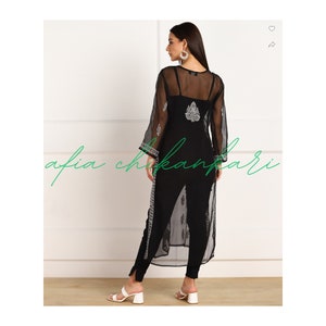 May include: A black sheer long-sleeved top with a white embroidered design. The top is worn over a black tank top and black trousers.