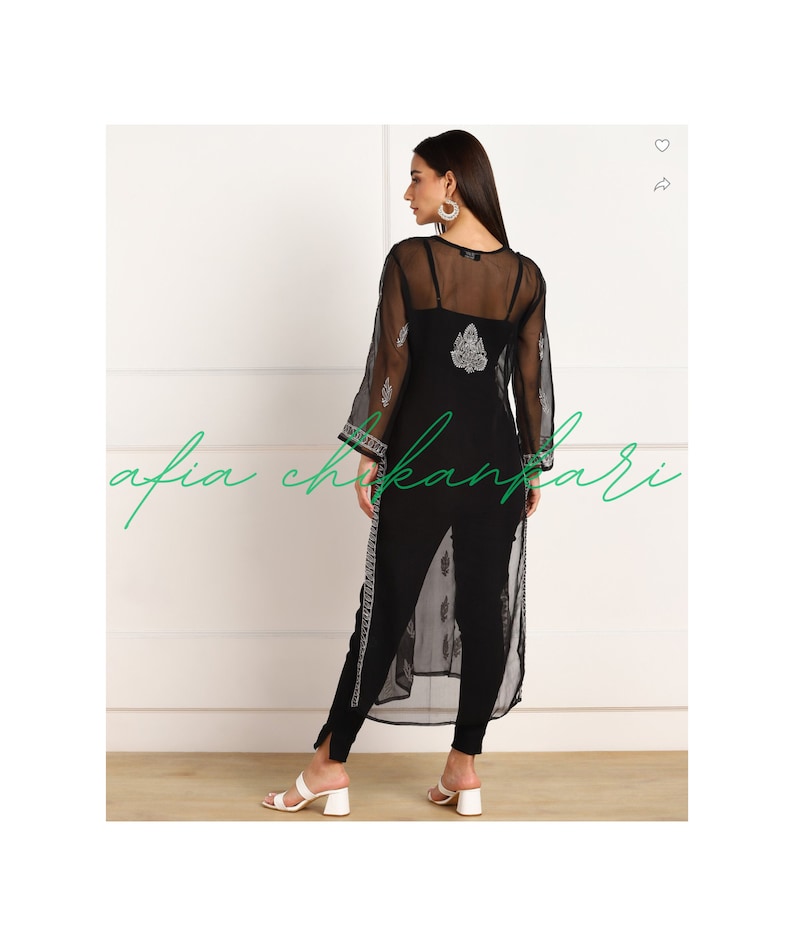 May include: A black sheer long-sleeved top with a white embroidered design. The top is worn over a black tank top and black trousers.