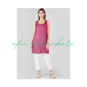Puede incluir: Una t&uacute;nica larga sin mangas de color magenta con un escote cuadrado. La modelo lleva pantalones blancos y sandalias blancas.