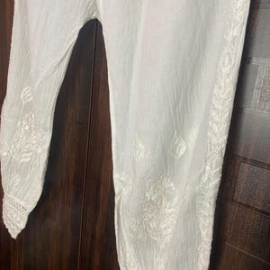 May include: White embroidered pants with a relaxed fit. The pants feature intricate floral embroidery along the sides and cuffs. The fabric appears lightweight and breathable, suitable for warm weather. The pants are made of a soft, flowing material.