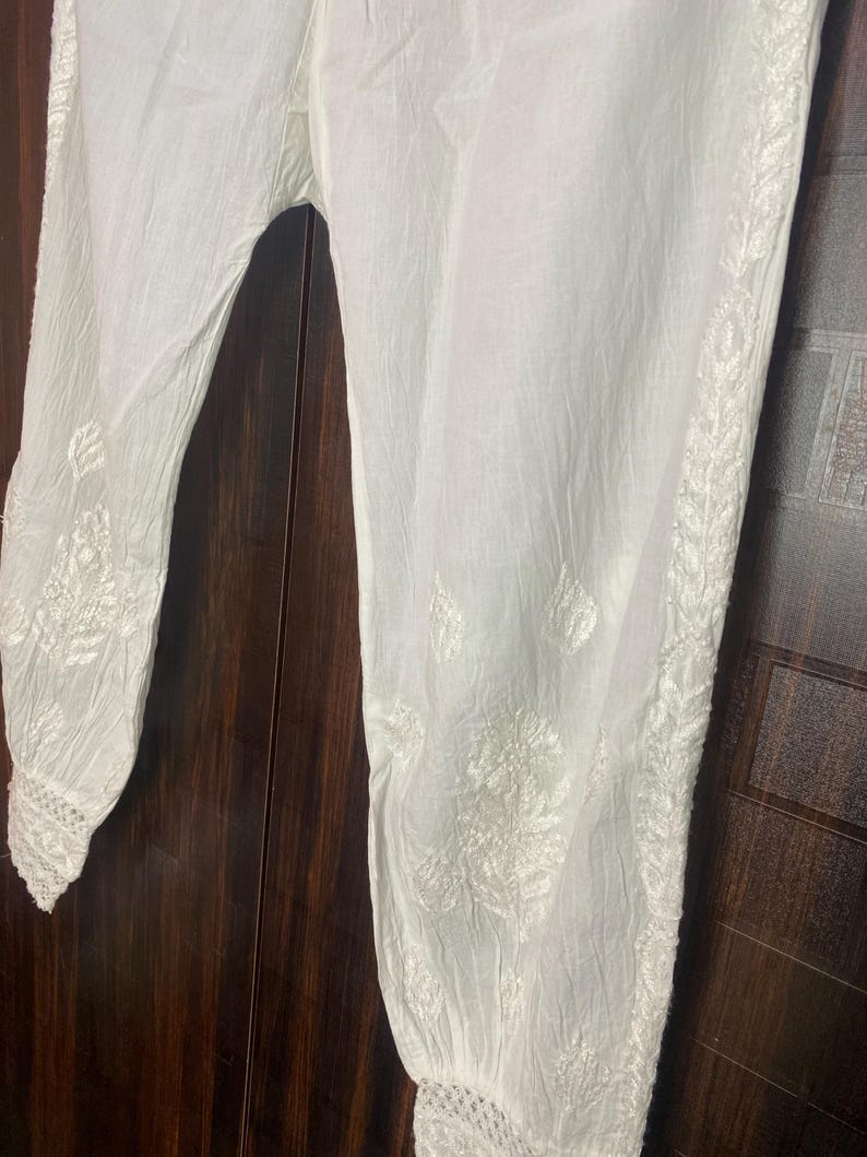 May include: White embroidered pants with a relaxed fit. The pants feature intricate floral embroidery along the sides and cuffs. The fabric appears lightweight and breathable, suitable for warm weather. The pants are made of a soft, flowing material.