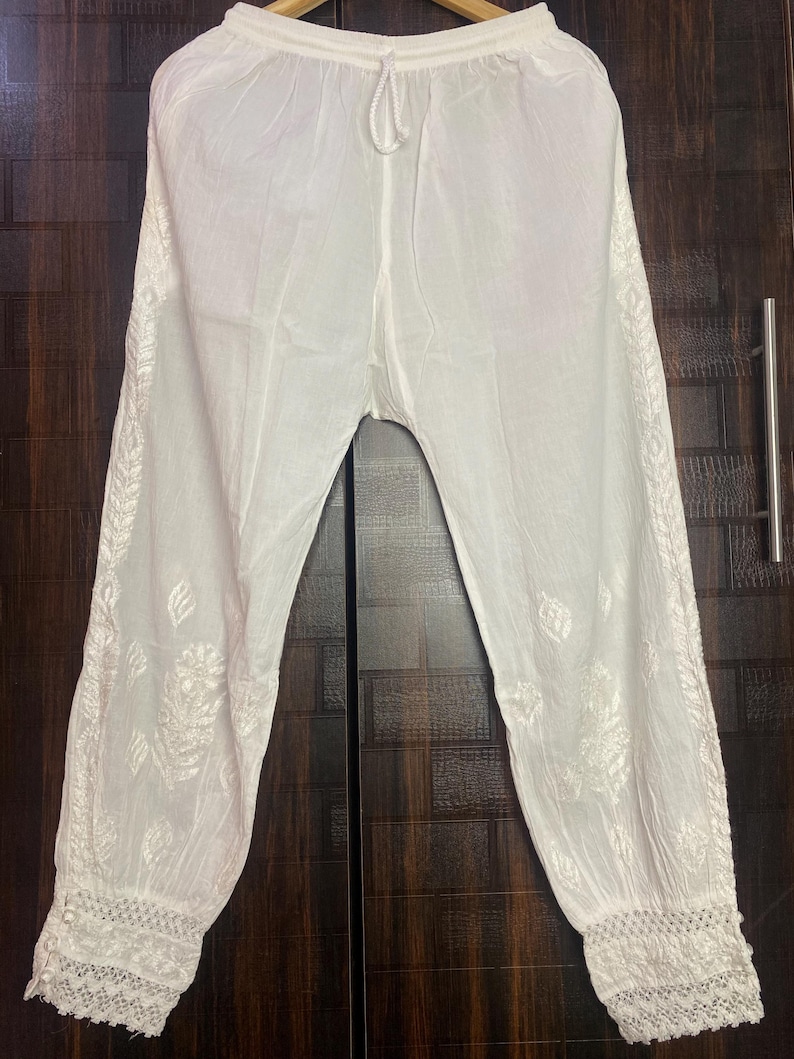 May include: White, lightweight pants with intricate embroidered floral patterns along the sides and at the cuffs. The pants have a drawstring waist and a relaxed fit, perfect for casual wear. The fabric appears to be a soft, breathable material.