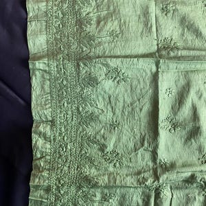 May include: A light green textile with intricate floral embroidery along one edge. The fabric has a slightly wrinkled texture, and the embroidery features detailed leaf and flower patterns. The overall aesthetic is delicate and handcrafted.