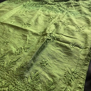 May include: A lime green tunic with intricate floral embroidery. The long-sleeved garment features detailed stitching around the neckline, sleeves, and hem. The fabric has a slightly textured appearance, and the overall design is elegant and detailed.