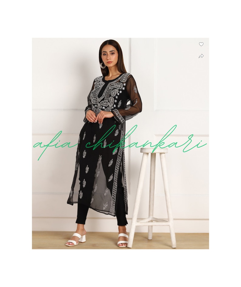 May include: A black sheer long-sleeved tunic with white embroidery. The tunic has a round neckline and a straight hem. The model is wearing black trousers and white sandals.