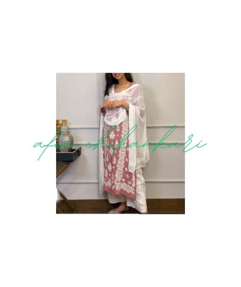 May include: A woman wearing a pink and white embroidered kurta with a white dupatta. The kurta has a floral design and the dupatta is sheer. The woman is standing in front of a white wall.