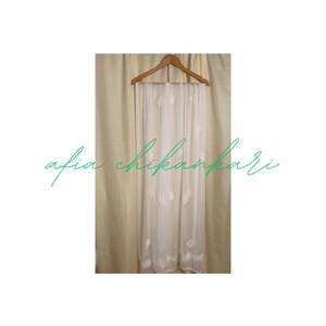 May include: White sheer scarf with delicate white embroidery. The scarf is hanging on a wooden hanger.