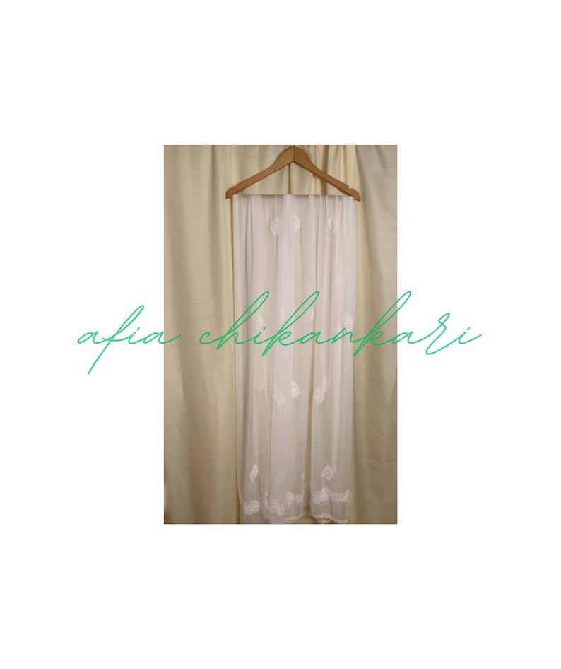 May include: White sheer scarf with delicate white embroidery. The scarf is hanging on a wooden hanger.