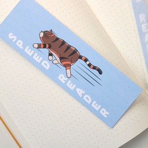 Può includere: Un segnalibro blu con un gatto dei cartoni animati che corre con il testo "Speed Reader" stampato su di esso.