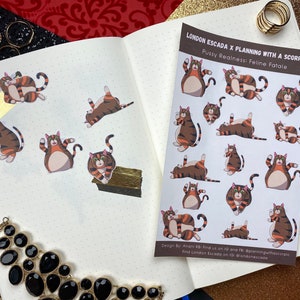 May include: A sheet of stickers featuring illustrations of brown and orange tabby cats in various poses. The stickers are titled "Pussy Realness: Feline Fatale" and are a collaboration between London Escada and Planning with a Scorpio.