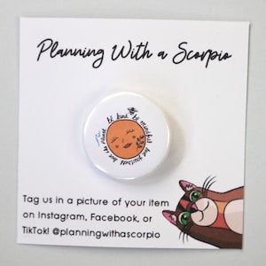 May include: White button with a brown and orange illustration of a face with the text "Be kind to the planet. Be mindful of yourself."  The button is on a white card with the text "Planning With a Scorpio" and a cartoon cat.