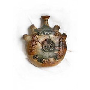 May include: A handcrafted ceramic flask with a rounded body and a small neck. The flask features a brown, green, and tan color scheme with embossed leaf and shell designs. It has three decorative protrusions and a textured surface.