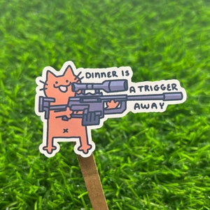 May include: A cartoon orange cat holding a rifle with a scope and the text "Dinner is a trigger away".