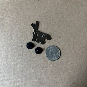 May include: A silver-colored metal pin in the shape of a rabbit, with two black pin backs and a US quarter for size comparison. The rabbit pin has a simple, stylized design.