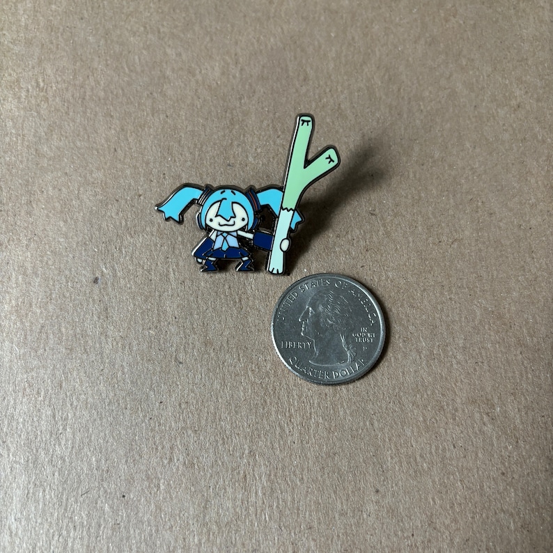 May include: Enamel pin featuring a cartoon character with blue hair and a dark blue outfit, holding a light green stalk. The pin is next to a quarter for size comparison. The pin has a black outline.