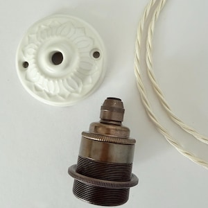 Könnte beinhalten: Ein weißer Deckenbaldachin aus Keramik mit floralem Reliefmuster, eine dunkelbronzene Metall-Lampenfassung mit Gewindeaußenseite und ein Stück weißes, gedrehtes Stoffkabel für eine Pendelleuchten-Montage.