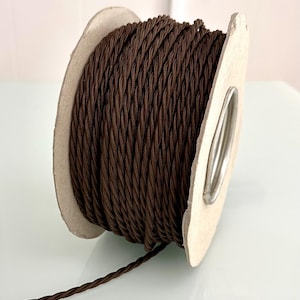 May include: A spool of dark brown twisted electrical wire. The wire is tightly wound around a cardboard core with a metal centre. The wire is a rich, chocolate brown colour and appears to be new.
