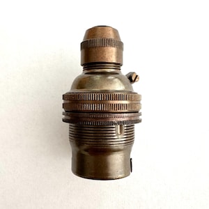 May include: A vintage lamp holder with a bronze finish. The holder features a ribbed design around the base and a textured top. A small screw is visible on the side. The design is industrial and classic, suitable for various lighting fixtures.