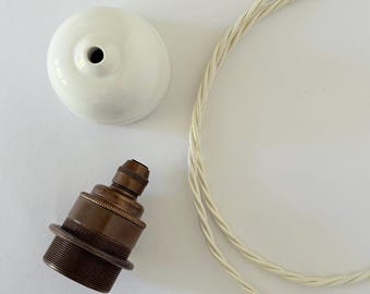 Rosone a cupola in ceramica bianca, portalampada E27 in ottone anticato, cavo in tessuto intrecciato.