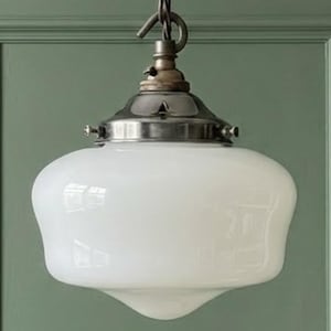 Op de afbeelding: Een hanglamp met een gladde, witte, ronde glazen kap bevestigd aan een metalen, zilverkleurige dop. De lamp hangt aan een metalen haak en kettingconstructie en heeft een strak, functioneel ontwerp.