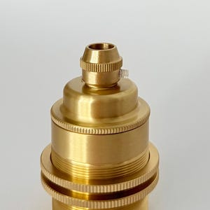 May include: A brass-colored lamp holder with a threaded base and a cylindrical body. The lamp holder has a textured surface and a small screw for securing a light bulb. The design is simple and functional.