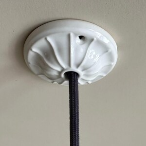 May include: White ceramic ceiling fixture with a black electrical cord hanging from it.