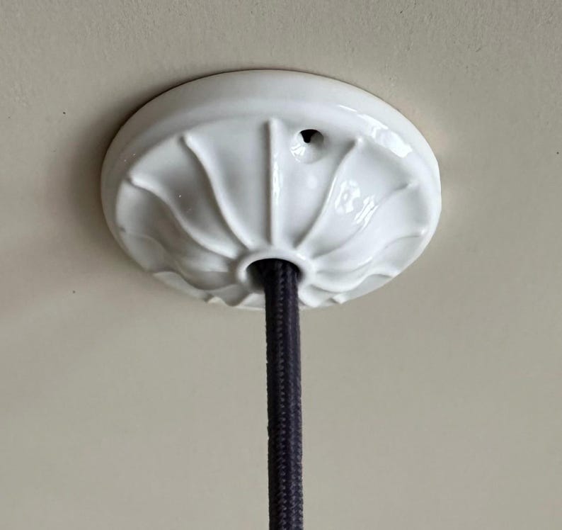 May include: White ceramic ceiling fixture with a black electrical cord hanging from it.