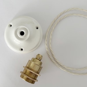 Op de afbeelding: Bovenaanzicht van een witte keramische plafondkap, een messing lamphouder en een lengte witte gedraaide elektriciteitskabel. De plafondkap heeft drie kleine gaten en een centrale opening. De lamphouder is cilindrisch.