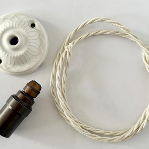 May include: A selection of vintage lighting parts. Includes a white ceramic ceiling rose with a floral pattern, a dark brown lamp holder, and a cream-coloured twisted fabric cable.