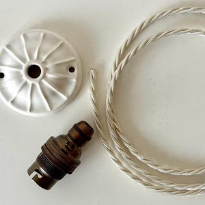 May include: A white ceramic ceiling rose with a radial design, a brown and brass lamp holder, and a silver twisted electrical cord. Components for a light fitting.