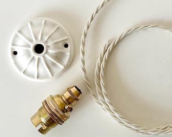 May include: A white ceramic ceiling rose with a radial pattern, a brass light bulb socket with a side switch, and a length of silver-colored twisted fabric electrical cord. These components are designed for assembling a pendant light fixture.