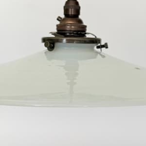 Op de afbeelding: Een hanglamp met een brede, ondiepe, doorschijnende witte glazen kap met een glad, taps toelopend profiel. De kap is bevestigd aan een donker, metaalkleurig bronskleurig armatuur aan de bovenkant, inclusief een centrale fitting en kleine schroeven.