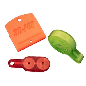 May include: Three 3D-printed plastic objects in orange, red, and green. The orange piece has the text "3D-FOX". The green piece is a rounded shape with a handle. The red piece has two circular holes.